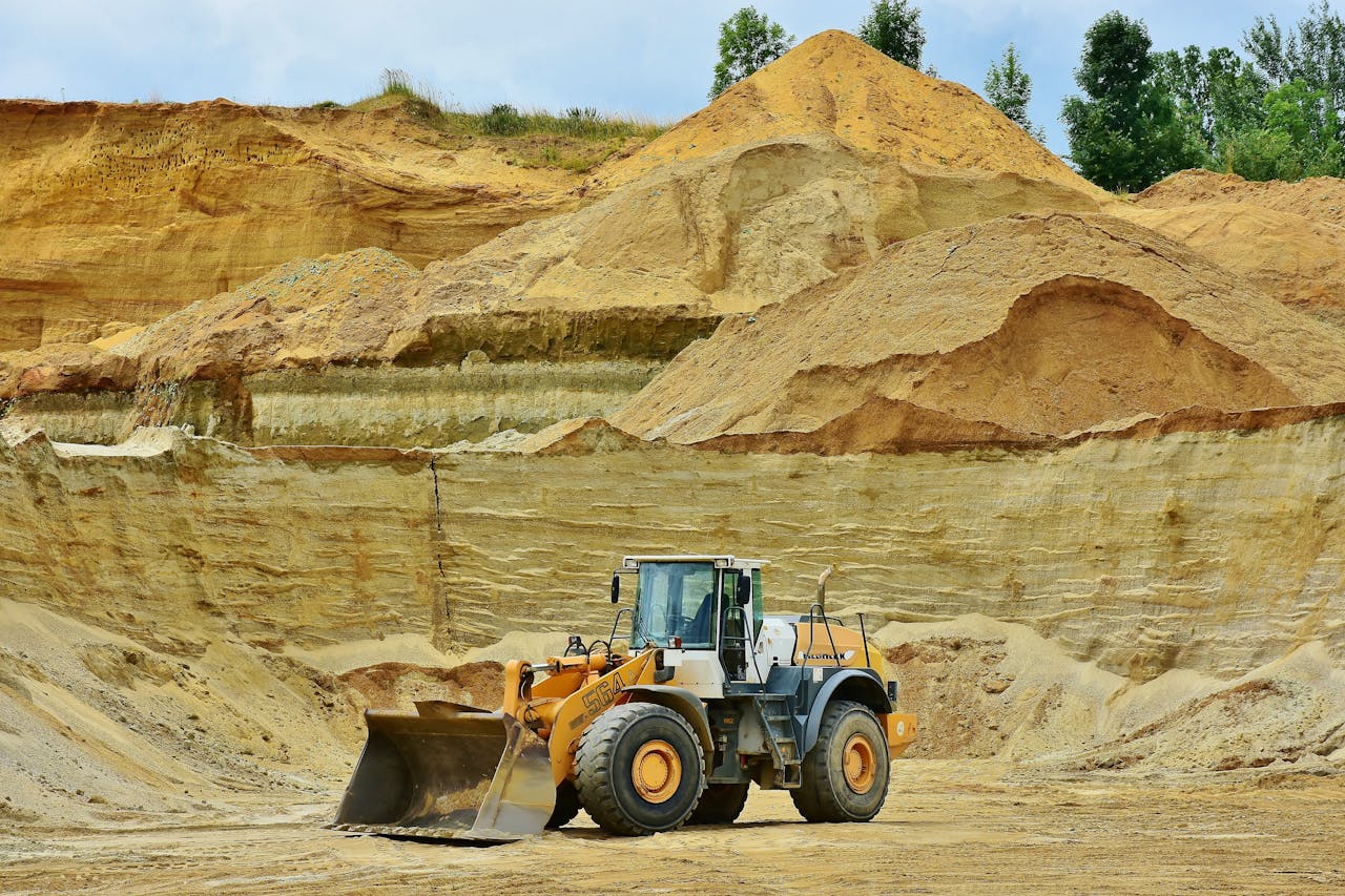 about-02 An excavator working in an open pit mine surrounded by sandy terrain and clear sky.