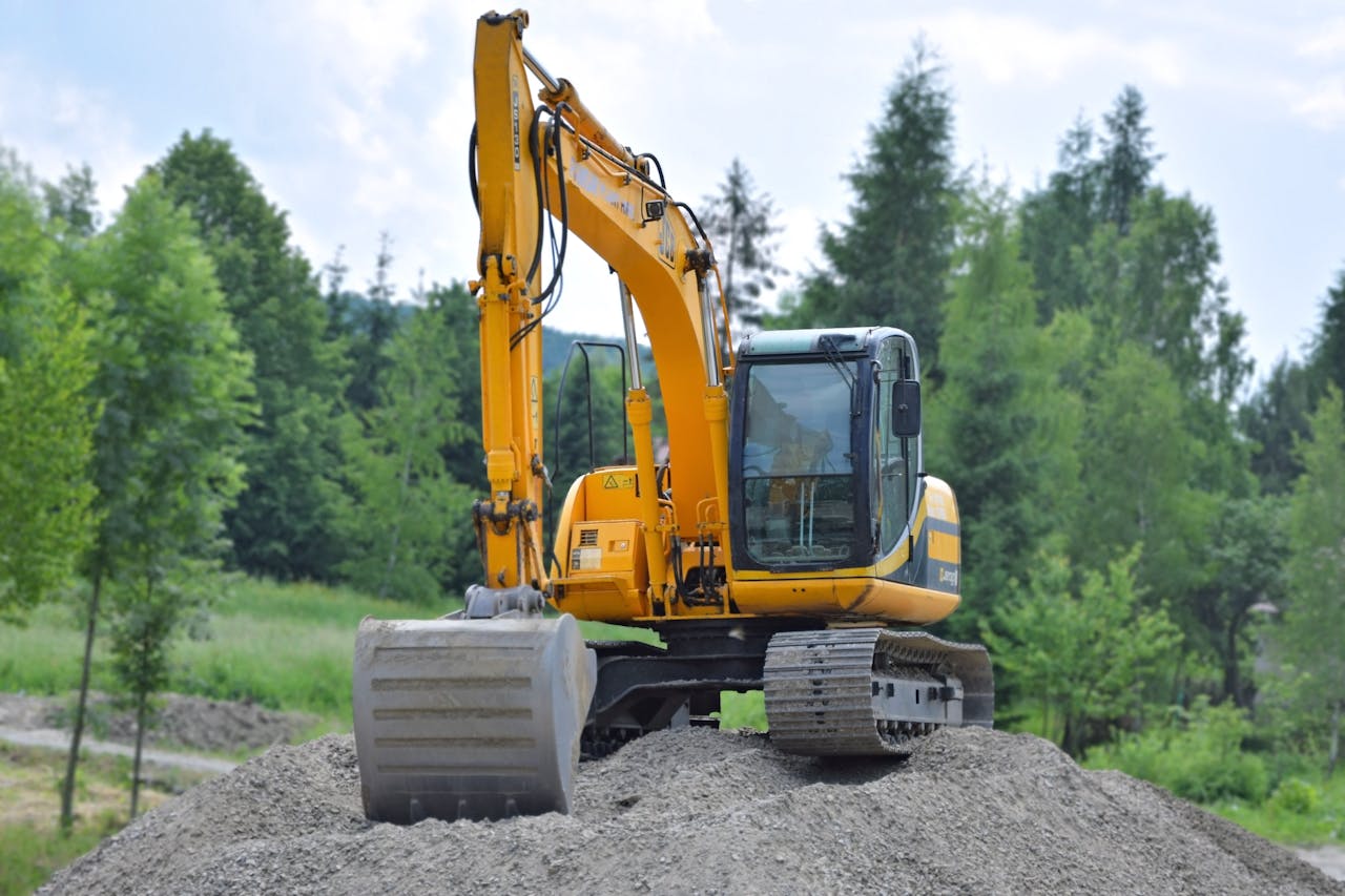 menu-01 A yellow excavator on a pile of gravel in a lush, green forest setting in Poland.